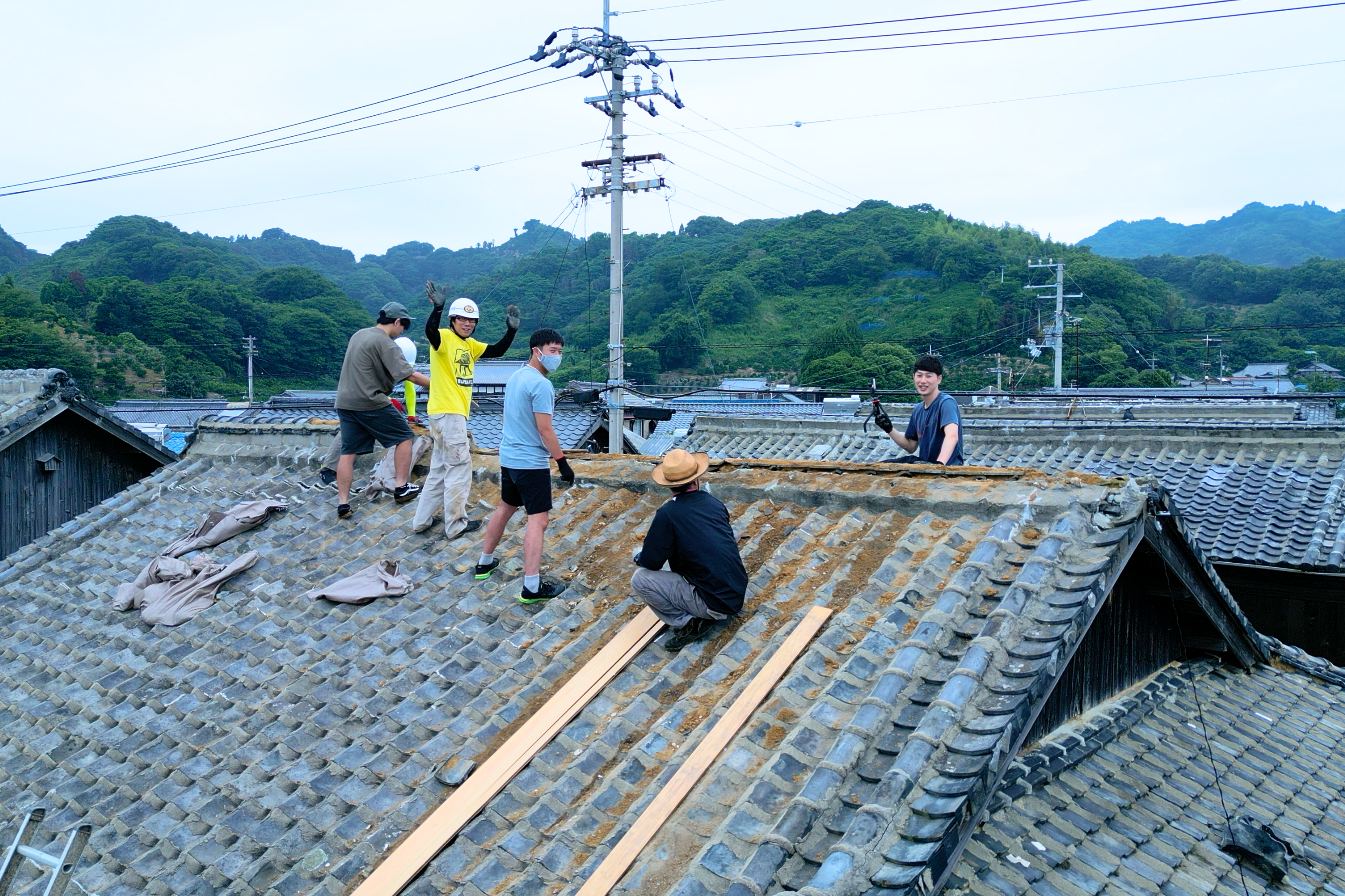 仲間と古民家の屋根瓦を下ろしている様子